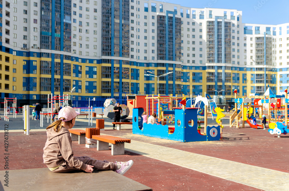 Obraz premium Little cute girl sits on the background of a large playground
