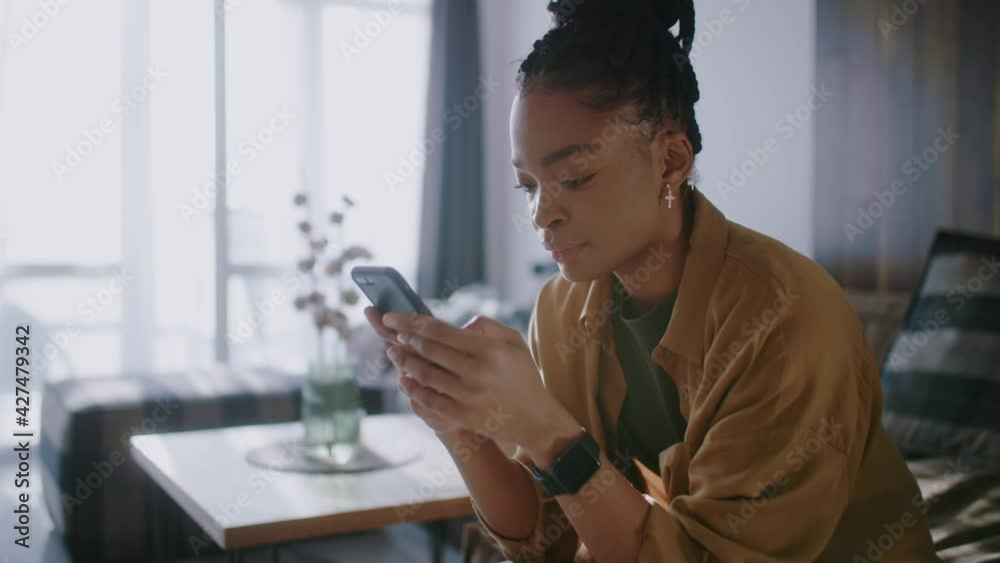 African american young woman in apartment texting chat messages mobile phone social media application in the morning. People. Technology. Lifestyle.