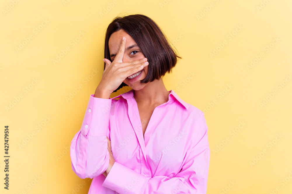 Young mixed race woman isolated on yellow background blink at the camera through fingers, embarrassed covering face. Young mixed race woman isolated on yellow background blink at the camera through fingers, embarrassed covering face.