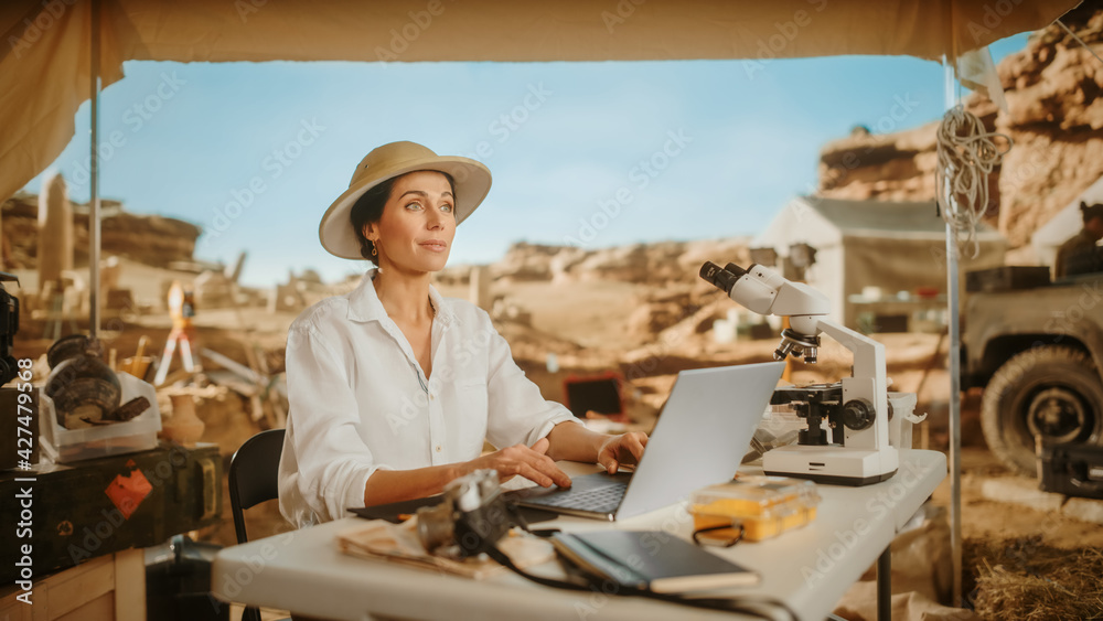 Archaeological Digging Site: Beautiful Female Archaeologist Doing Research, Using Laptop, Analysing Fossil Remains with Microscope. Historians Excavating Site of Great Diverse Ancient Civilization