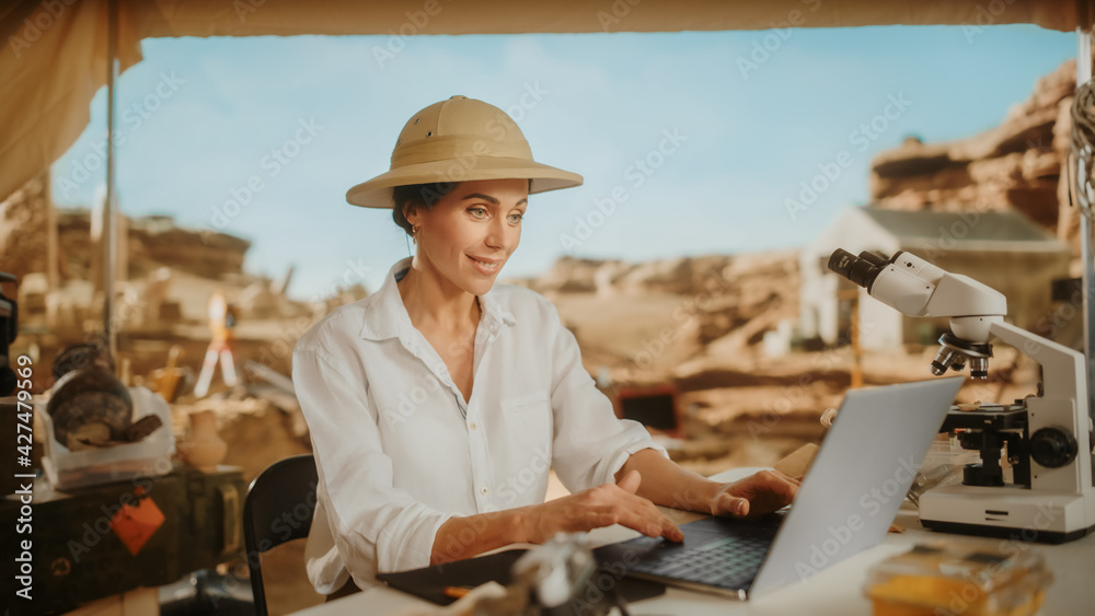 Archaeological Digging Site: Famous Female Archaeologist Doing Research, Using Laptop, Analysing Fossil Remains, Ancient Civilization Culture Artifacts. Team of Historians work on Excavation Site