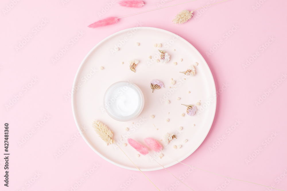 Jar of cosmetic cream with dry flowers on pink background Jar of cosmetic cream with dry flowers on pink background
