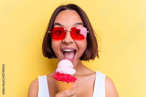 Young mixed race woman holding an ice cream isolated on yellow background