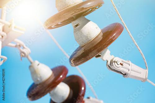 A ceramic suspended insulator hangs from a power line against a blue sky. photo