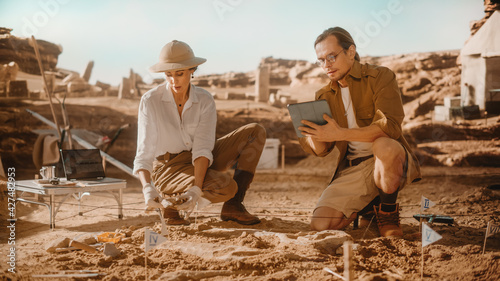 Archaeological Digging Site: Two Great Paleontologists Use Tablet Computer to Analyse Skeleton of Newly Discovered Dinosaur. Archeologists on Excavation Site Discover Fossil Remains of New Species