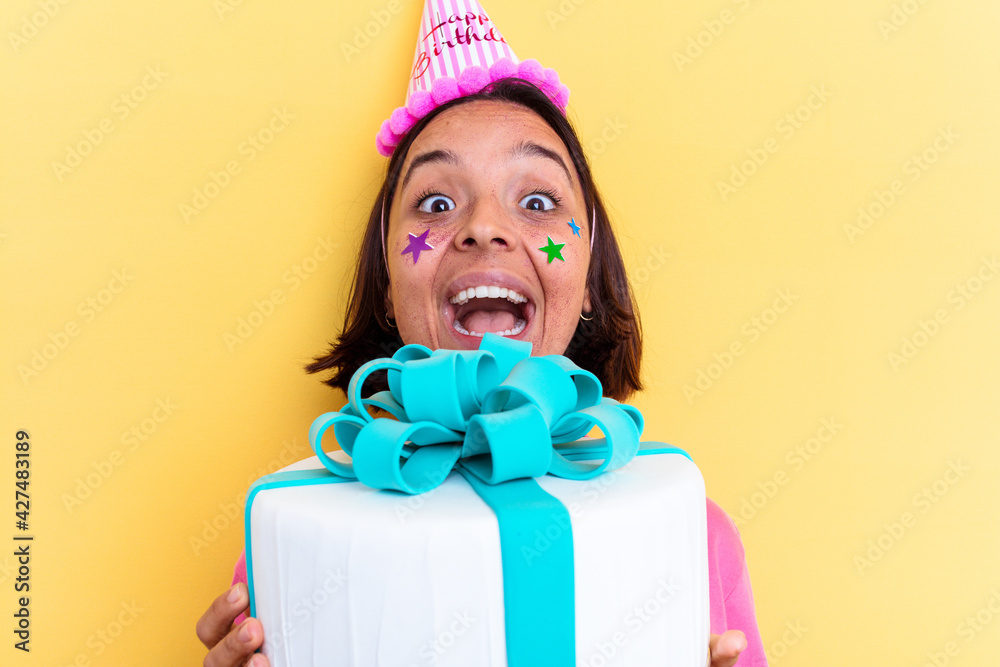 Young mixed race woman holding a birthday cake isolated on yellow background Young mixed race woman holding a birthday cake isolated on yellow background
