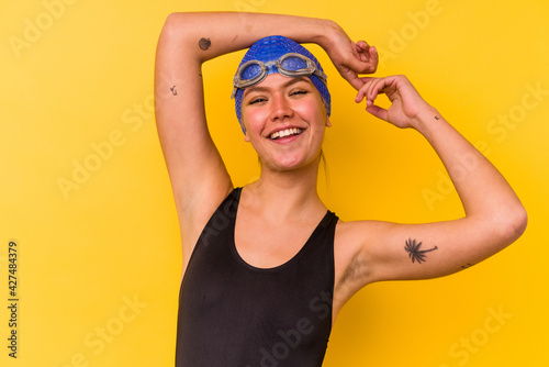 Young swimmer venezuelan woman isolated on yellow background stretching arms, relaxed position.