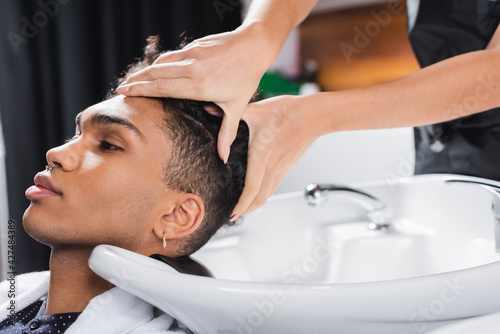 Hairstylist washing head of african american client near sink in salon