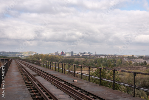 Railway tracks on a bridge, view of an industrial area under a cloudy sky