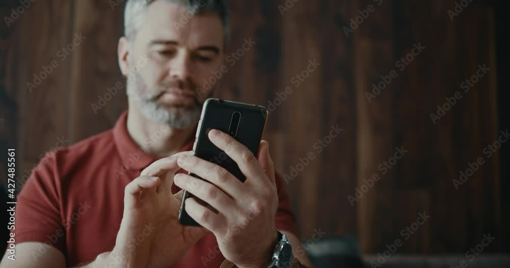 Caucasian bearded adult millennial with mobile phone typing messages to busiess partner communicating social media application sharing news online.