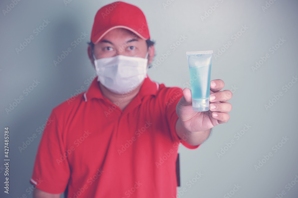Close-up focus at alcohol gel in hands Asian deliveryman wearing red cap and mask medical, red uniforms to prevent coronavirus that is currently spreading. Concept protection virus, health take care. Close-up focus at alcohol gel in hands Asian deliveryman wearing red cap and mask medical, red uniforms to prevent coronavirus that is currently spreading. Concept protection virus, health take care.