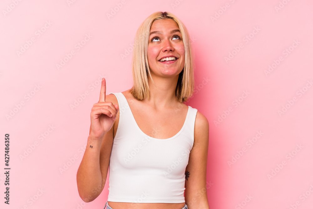Young venezuelan woman isolated on pink background indicates with both fore fingers up showing a blank space.
