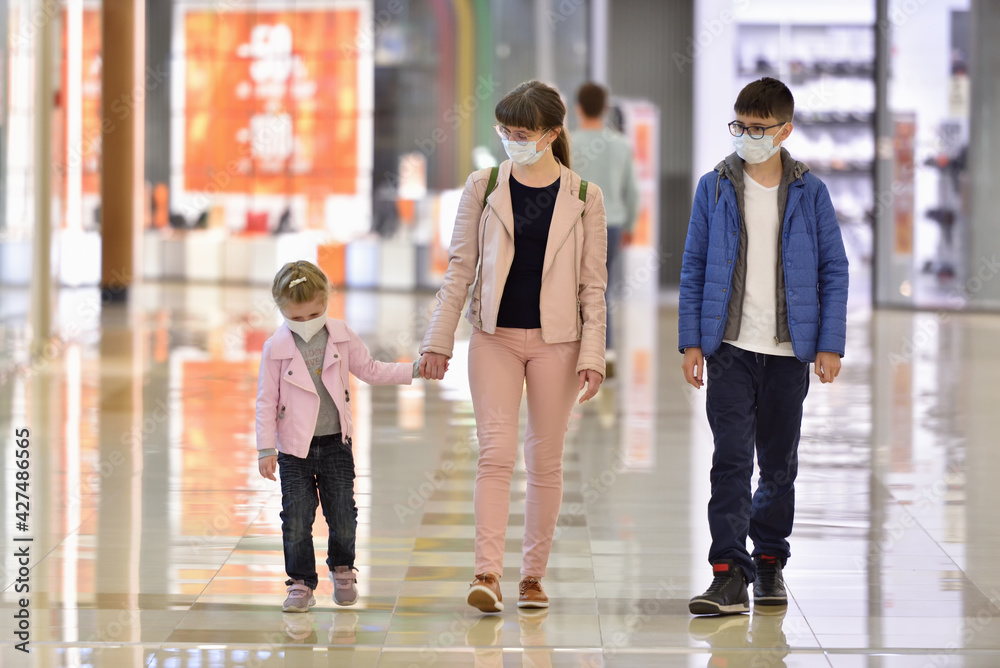 Fototapeta premium Mom and children wearing face masks walk through the shopping center during the COVID-19 pandemic.