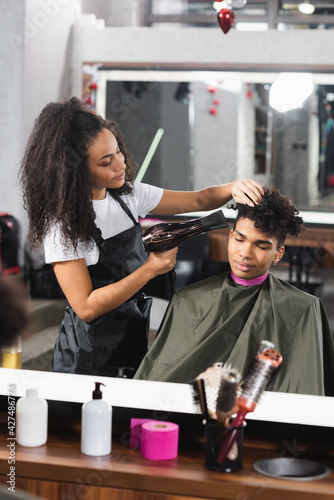 African american hairdresser using hair dryer while working with client