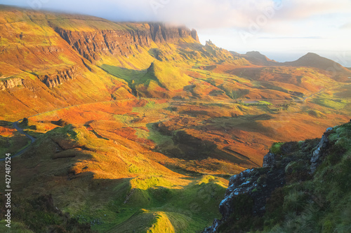 Vibrant golden light at sunset or sunrise over colourful landscape view of the rugged, otherworldly terrain of the Quiraing on the Isle of Skye, Scotland.