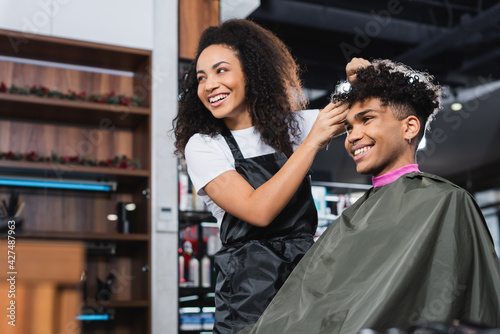 Cheerful african american hairstylist and client looking away in salon