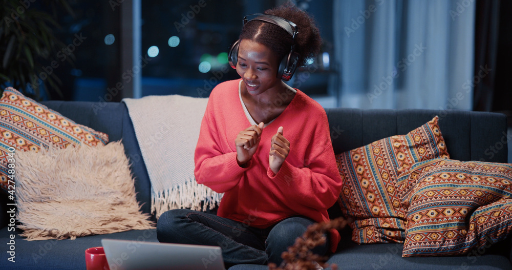 Obraz premium Lovely african girl talk webcam with friend wearing headphones dancing together into music videochatting in laptop. Candid lifestyle. Communications.