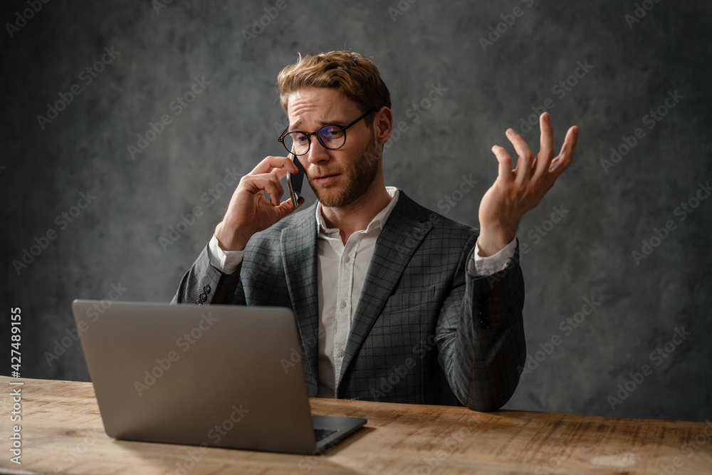 The wrinkling forehead man talking on the phone while looking into laptop screen in the studio The wrinkling forehead man talking on the phone while looking into laptop screen in the studio