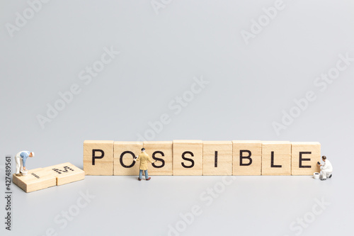 Miniature  people worker team on impossible word in wooden alphabet letters with prefix un crossed out, leaving the word possible