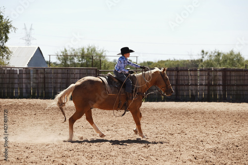 Young cowboy riding palomino horse through outdoor arena for western lifestyle on ranch.