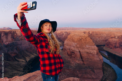 blonde girl makes selfie on Horseshoe Bend in Glen Canyon National Recreation Area in early dawn