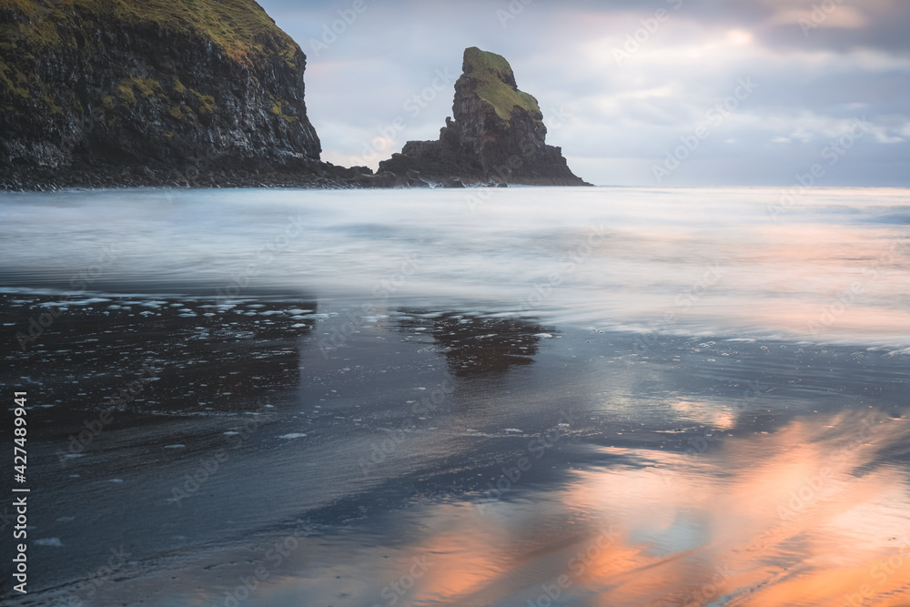 Idyllic seascape and sea stack with wet sand reflection during sunrise or sunset at Talisker Bay Beach on the Isle of Skye, Scotland