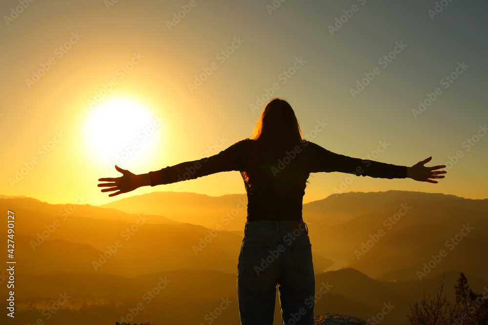 Back silhuette of a woman spreading with open arms at sunset