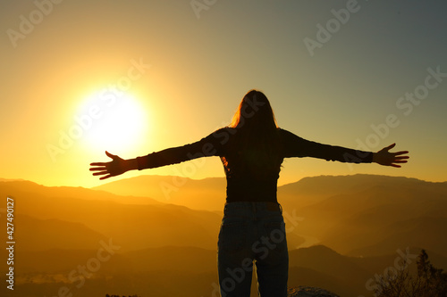 Back silhuette of a woman spreading with open arms at sunset