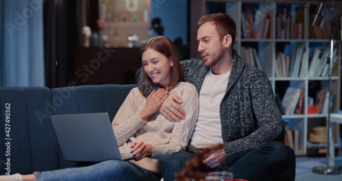 Affectionate young caucasian couple of girlfriend and boyfriend lying on couch together using mobile phone watching videos communication online.