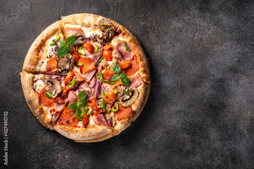 Hot pizza with pepperoni, mozzarella, mushrooms and bacon on a dark background, copy space, horizontal orientation, flat lay