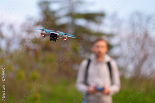 Small drone flying hanging in the air with man who navigates it in the background. Selective focus, blurred background. New technology, devices, gadgets concept.