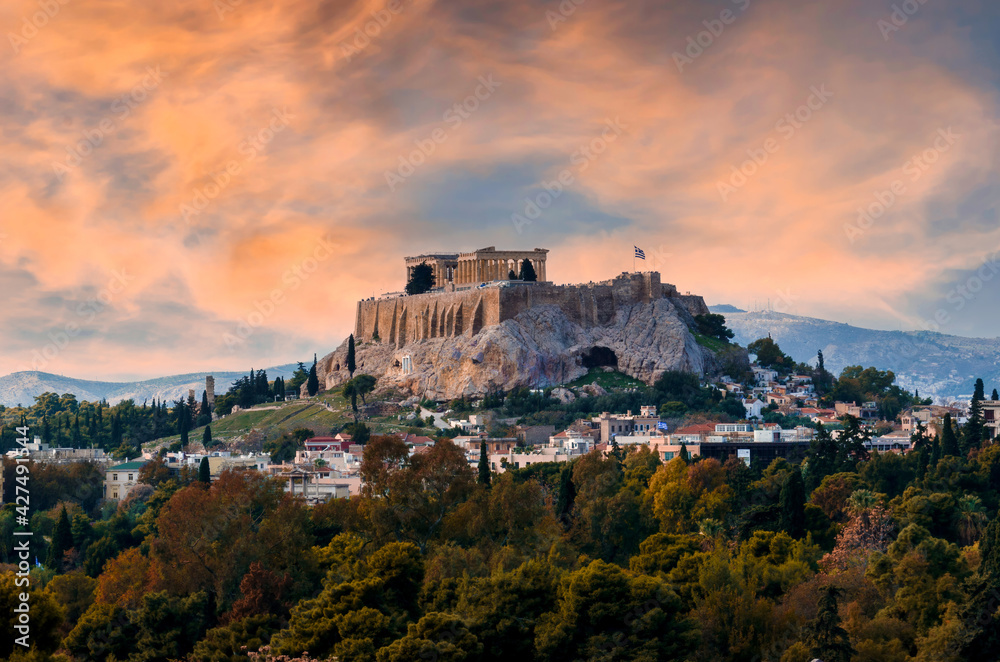 The Acropolis of Athens city in Greece with the Parthenon Temple (dedicated to goddess Athena), at sunset time with colorful cloudy sky. Plaka district under the Acropolis. Scenic urban view at dusk
