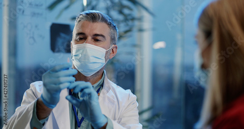 Caucasian grey haired professional doctor microbiologist doing antiviral vaccine against disease for female customer patient in private clinic laboratory.