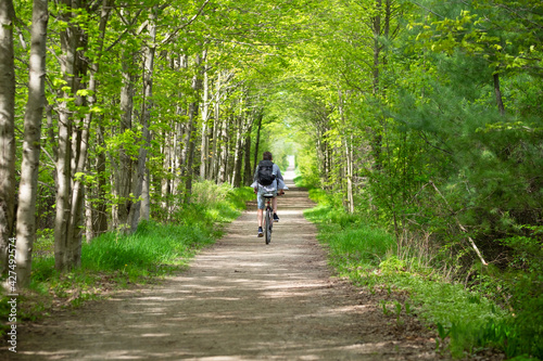 Young man biking cycling through the park alley green tunnel made of tree brunches. Summer, spring scene. Recreational sport and cycling concept. Selective focus. Caledon trailway path, Ontario.