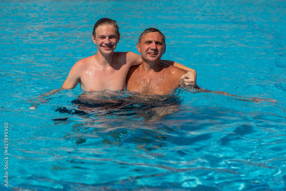Real people concept, beautiful young man and teenage boy swimming and having fun in pool in vacation. happiness and nice body for enjoyed people live an alternative lifestyle . Father hugging son.