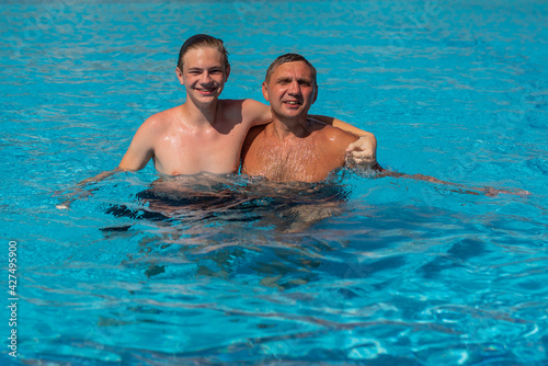 Real people concept, beautiful young man and teenage boy swimming and having fun in pool in vacation. happiness and nice body for enjoyed people live an alternative lifestyle . Father hugging son.