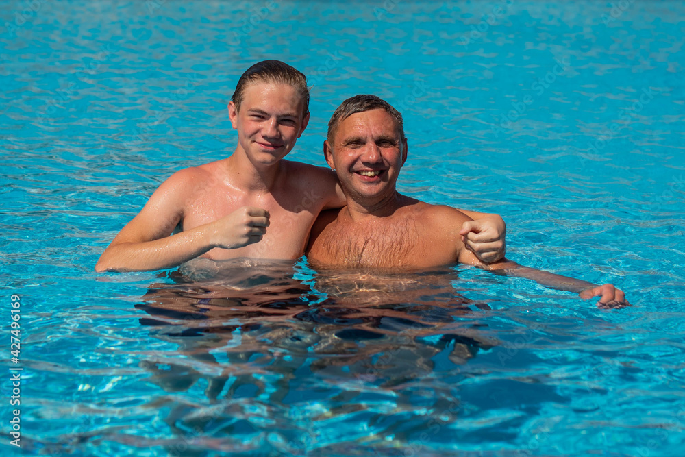 Real people concept, beautiful young man and teenage boy swimming and having fun in pool in vacation. happiness and nice body for enjoyed people  lifestyle as vacation. Father hugging son.