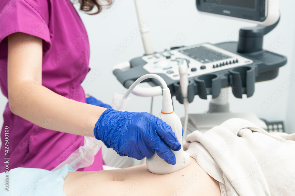 Ultrasound examination. The doctor's gloved hand with an ultrasound sensor on the patient's abdomen closeup.