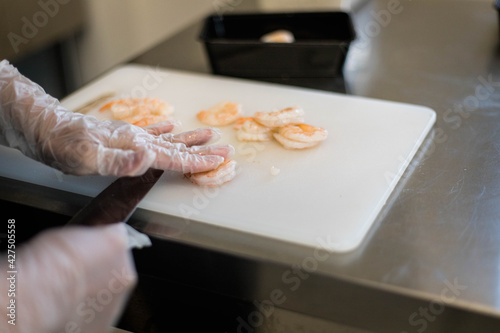 mains de Femme qui prépare des crevettes dans un restaurant avec un couteau et des gants photo