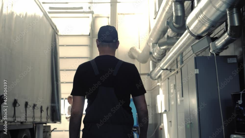 A mechanic in overalls walks through the workshop along a cargo trailer. Truck service station everyday life