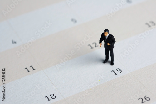 Selective focus miniature businessman standing on calendar checking schedule.