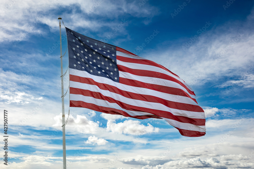 Obraz premium USA flag on a pole waving against blue cloudy sky background.