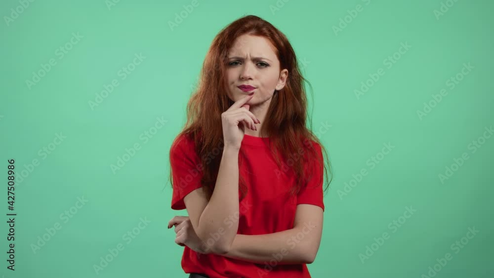 Thinking woman looking up on green studio background. Pensive face expressions. Pretty model with attractive appearance and red natural hair. Thinking woman looking up on green studio background. Pensive face expressions. Pretty model with attractive appearance and red natural hair.