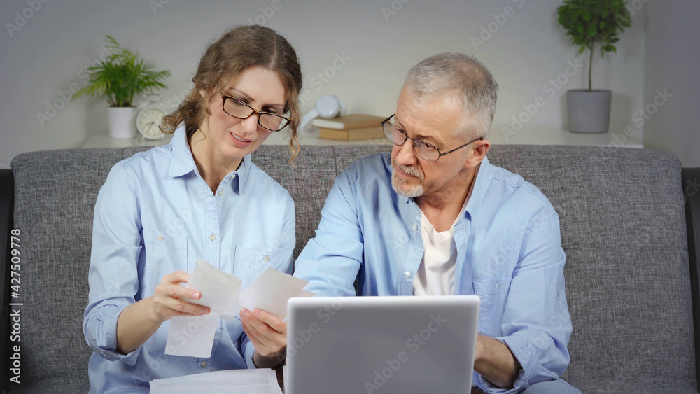 A married couple discusses financial expenses on a laptop.