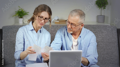 A married couple discusses financial expenses on a laptop.