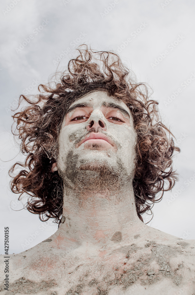 portrait of young man with half hair with face covered in mud