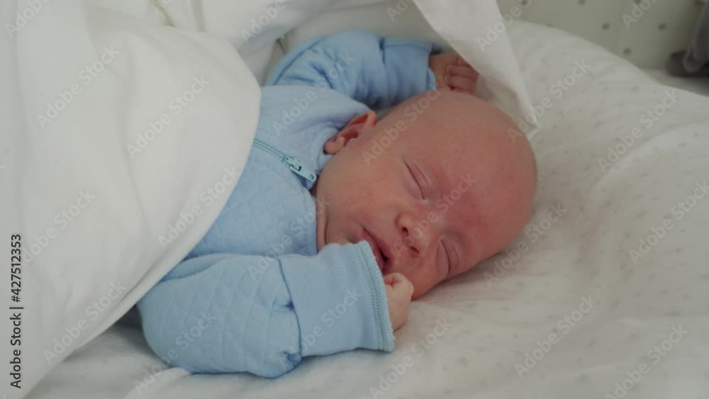 Newborn baby boy in jumpsuit is sleeping peacefully in bed, 1 month old infant waking up, lying in baby pod nest cocoon at home. High quality 4k footage Newborn baby boy in jumpsuit is sleeping peacefully in bed, 1 month old infant waking up, lying in baby pod nest cocoon at home. High quality 4k footage