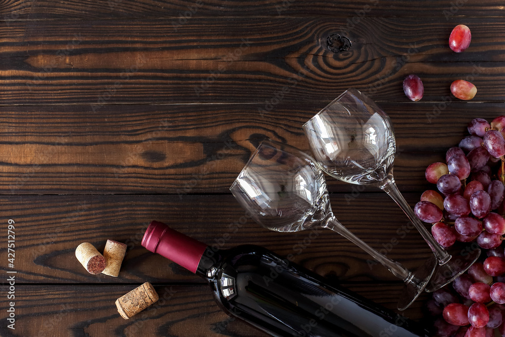 top view of glasses and a bottle of red wine, a bunch of ripe grapes on a dark wooden table. horizontal layout with space for text