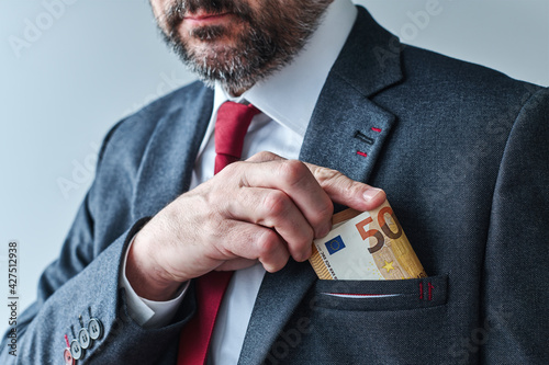 Businessman putting euro cash money into his suit pocket photo