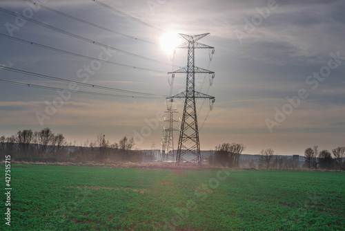 Linia elektryczna wysokiego napięcia oświetlona promieniami słonecznymi.